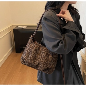 Chic leopard print shoulder bag with brown leather strap worn over a woman's shoulder