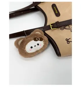 Detail of cute cat plush charm with pink bow and metal chain on a brown tote bag