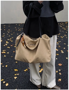 Detail of khaki canvas hobo tote featuring black shoulder strap and wooden bead charm