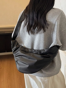 Minimalist black crescent crossbody bag with wide strap worn by a model in casual style