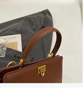 Détail d'un sac à main en cuir marron avec fermoir pivotant doré et poignée supérieure ronde