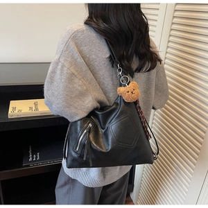 Detail of black PU tote bag side zipper with plush bear charm and plaid scarf accent