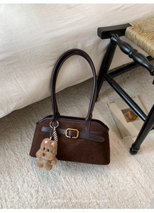 Dettaglio borsa a spalla in pelle scamosciata marrone con fibbia dorata e ciondolo a peluche