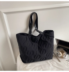 Detail of quilted S-pattern on black tote bag with long leather handles in a workspace setup