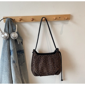 Detail of leopard print shoulder bag hanging on a wooden rack with lifestyle accessories
