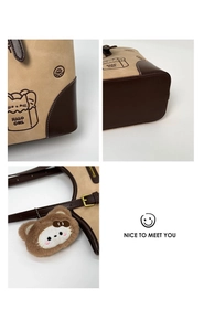 Detail of khaki tote bag featuring cat illustration, leather trim and plush charm accessory
