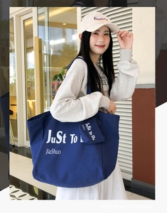 Close-up of blue canvas tote bag with letter print and matching zipper pouch charm