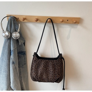 Detail of leopard print shoulder bag with black leather strap on wooden hook