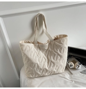 Detail of cream quilted tote bag featuring unique S-shape embossed pattern and brand label