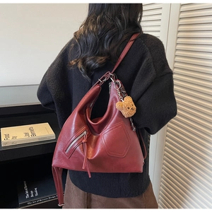 Close-up of burgundy leather tote bag featuring side zipper pocket and fringe tassel detail