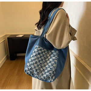 Détail du grand sac cabas en denim bleu avec patch à damier porté sur un manteau beige