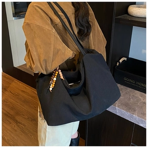 Detail of black canvas tote bag with brown leather straps and wooden bead charm