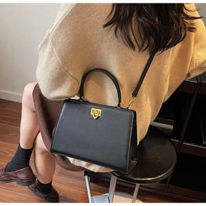 Close-up of black leather handbag with golden U-shaped clasp shown in lifestyle setting