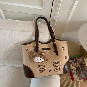 Detail of khaki tote bag with cute cat prints and plush bear pendant on a white sofa
