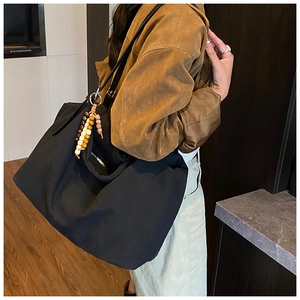 Detail of a large black canvas tote bag with colorful bead pendant on model shoulder