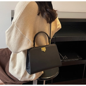 Detail shot of a black vintage handbag worn over the shoulder with gold square lock buckle
