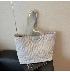 Detailed view of light gray quilted tote bag with S-shape stitching and rubber brand label