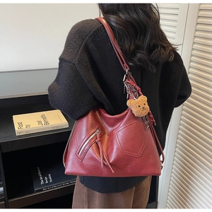 Detail of dark red soft leather hobo bag with teddy charm and zip pockets on shoulder