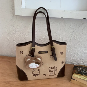 Detail of a beige and brown tote bag with cat illustrations and a plush charm