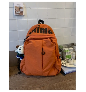 Detalle de la mochila naranja resistente al agua con letras KIMA y colgante de peluche