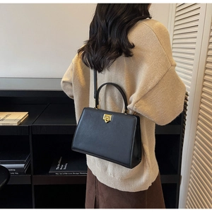 Close-up of a black leather crossbody bag with a gold lock, worn by a model in a library