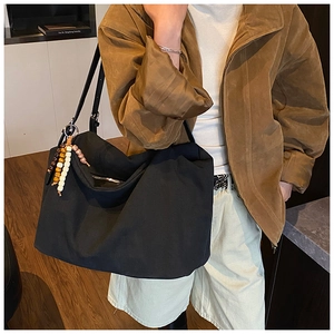 Detail of black canvas tote bag with beaded tassel charm on a stylish model's shoulder
