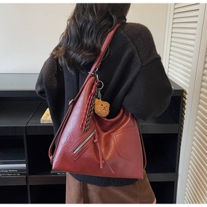Detail view of burgundy faux leather tote bag with long tassels and plush bear pendant
