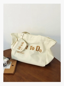 Detail of canvas tote bag with letter print and small pouch on a wooden desk