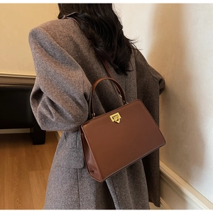 Brown vintage leather handbag with gold twist lock worn by a model in a warm blazer