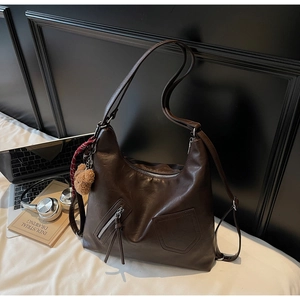 Detail of deep brown faux leather tote bag with silver zippers and plush bear accessory