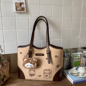 Detail of beige tote bag featuring embroidered cat motif and plush charm on wooden table