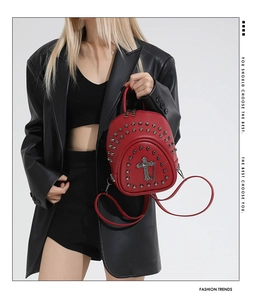 Red leather mini backpack with silver rivets and gothic cross pendant held by a model