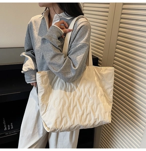 Detail of the large tote bag showing minimalist S-shaped quilted pattern and soft off-white fabric