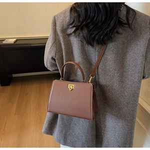 Close-up of brown leather handbag featuring a golden turn-lock buckle and slim shoulder strap