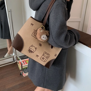 Close-up of khaki and brown tote bag with cute cat illustrations and plush animal charm