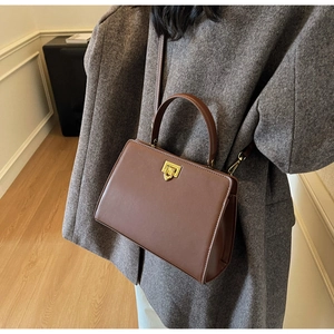 Detail of vintage brown leather handbag with gold metal lock on casual wool coat