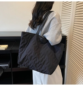 Detail of black quilted tote bag with S-shaped stitching and leather JUM decorative tag