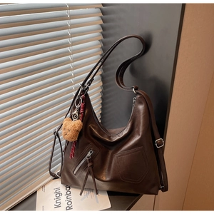 Detail of dark brown hobo shoulder bag with wax leather texture and plush bear charm