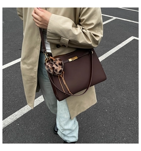 Detail of dark brown leather handbag featuring a gold twist lock and leopard heart charm
