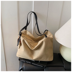 Detail of khaki tote bag with black leather straps and wooden bead charm on leather bench