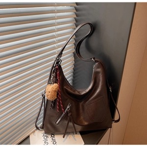 Detail of dark brown faux leather tote bag with plush bear charm and metallic zippers