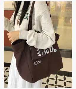 Detail showing deep brown canvas tote bag with white lettering on long shoulder strap