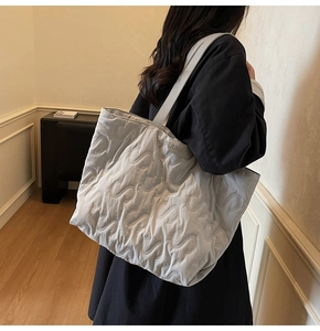 Side view of large light grey quilted tote bag with S-shape stitching on model shoulder