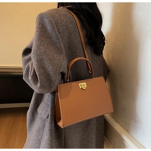 Detail of caramel leather square bag with gold lock and top handle on grey blazer