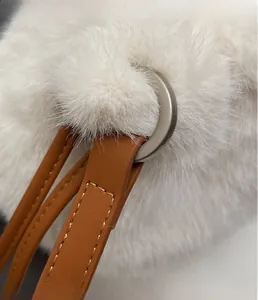 Detail of white plush bucket bag showing brown leather strap and silver metal buckle
