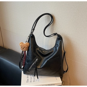 Detail of black leather tote bag with silver zippers and a brown plush bear keychain