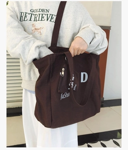 Close-up of brown canvas tote bag featuring white letter D print and external zipper pocket