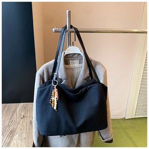 Detail of black canvas tote bag with retro beaded charm and leather shoulder strap