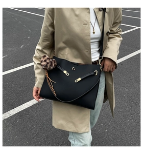 Black cross-grain leather tote bag detail with gold lock and leopard print pom-pom charm