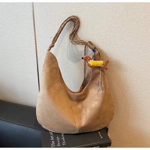 Detail of a brown suede hobo bag with a woven rope handle and a small dog plush pendant